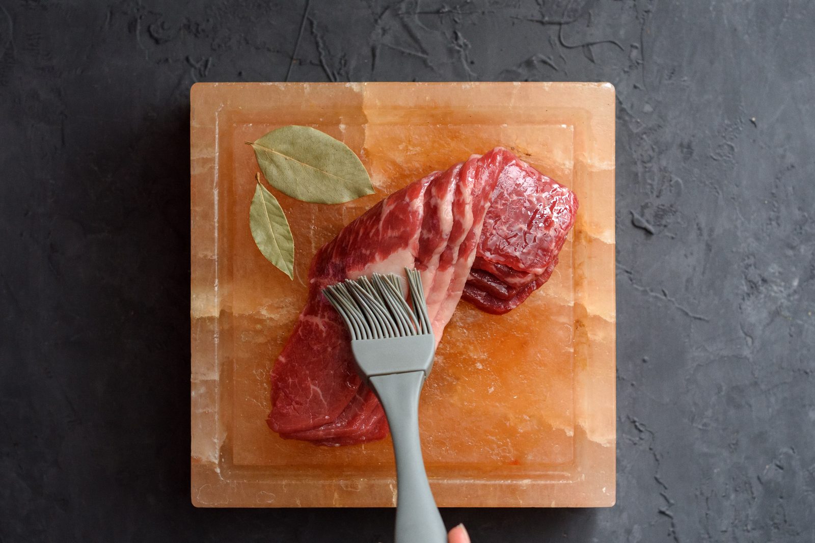 Raw beef being brushed on a Himalayan salt cooking slab